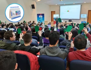 Estudiantes en el salón de actos levantando tarjetas verdes y rojas, en una actividad gamificada. Se muestra en un círculo un calendario como obsequio para los asistentes