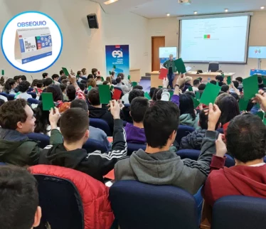 Estudiantes en el salón de actos levantando tarjetas verdes y rojas, en una actividad gamificada. Se muestra en un círculo un calendario como obsequio para los asistentes
