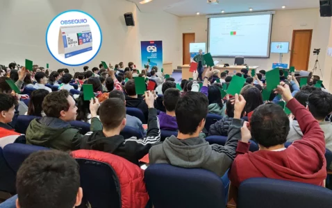 Estudiantes en el salón de actos levantando tarjetas verdes y rojas, en una actividad gamificada. Se muestra en un círculo un calendario como obsequio para los asistentes