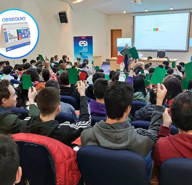 Estudiantes en el salón de actos levantando tarjetas verdes y rojas, en una actividad gamificada. Se muestra en un círculo un calendario como obsequio para los asistentes