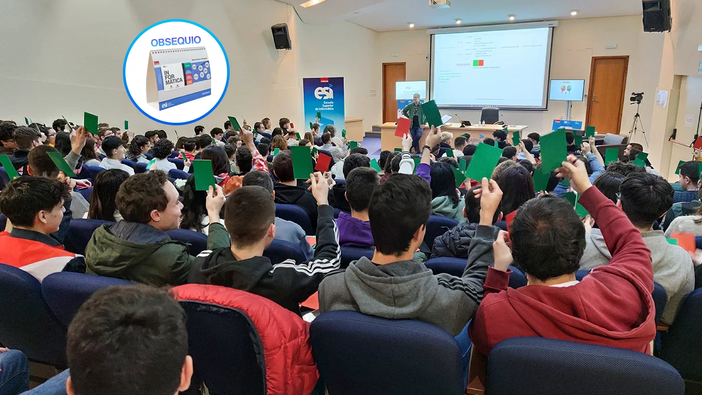 Estudiantes en el salón de actos levantando tarjetas verdes y rojas, en una actividad gamificada. Se muestra en un círculo un calendario como obsequio para los asistentes