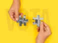 Hände halten Puzzleteile mit einem Teil der ESI-Fassade. Hinter dem Wort ABSTIMMUNG