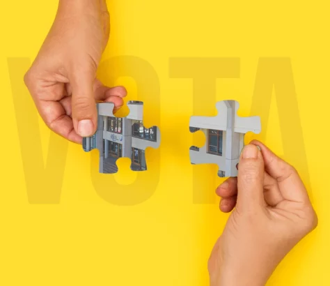Hands holding puzzle pieces with part of the ESI facade. Behind the word VOTE