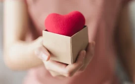 Woman holding a cardboard box on which there is a red heart