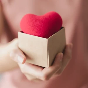 Mujer sujetando una caja de cartón sobre la que hay un corazón rojo